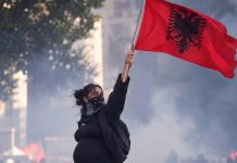 Një grua shtatzënë lartëson flamurin kombëtar në mes të tymit dhe protestave në Tiranë
